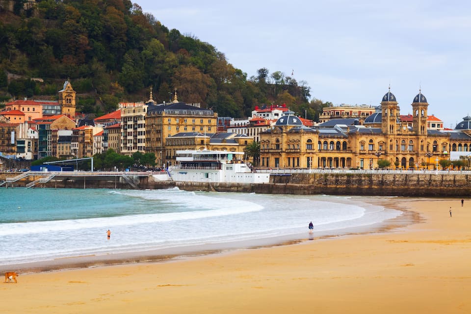 A coastal cityscape with historic buildings, a beach, and a boat docked near the shore.