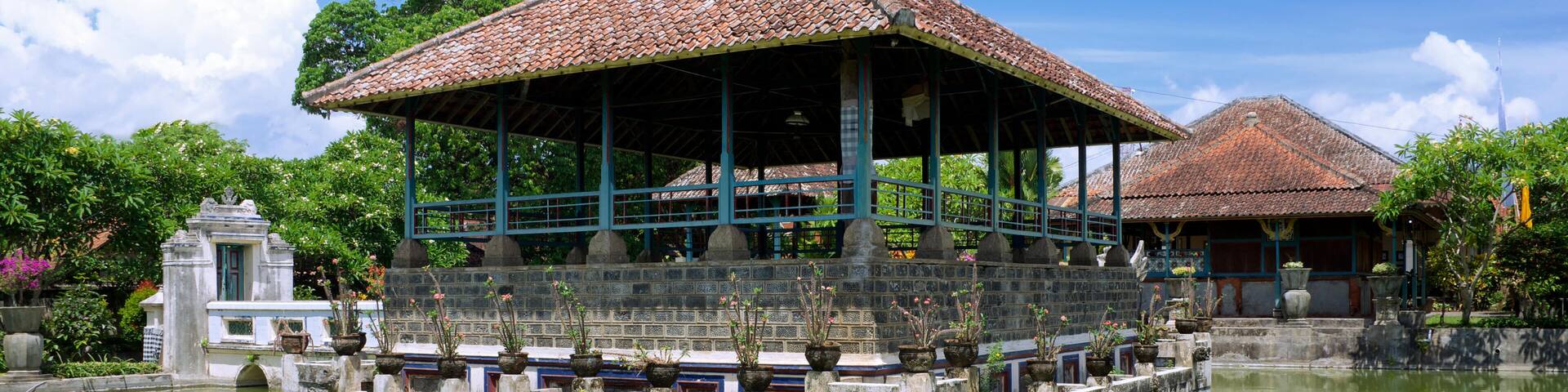 A traditional pavilion with a tiled roof, surrounded by a stone wall and a calm pond.