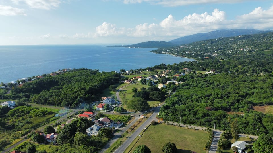 A coastal town with a clear view of the sea, surrounded by lush greenery and hills.