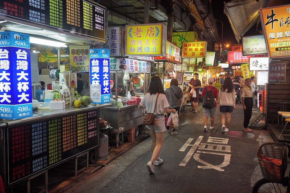 A bustling street market with various food stalls and signs in a foreign language.