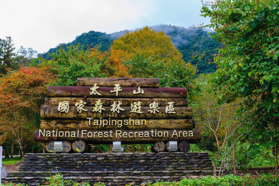 A sign for Taipingshan National Forest Recreation Area with a backdrop of autumn foliage and mountains.