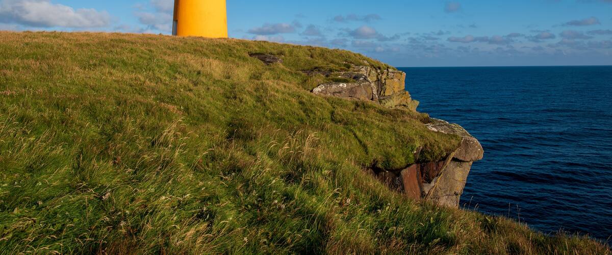 A yellow lighthouse on a grassy cliff overlooking the ocean.