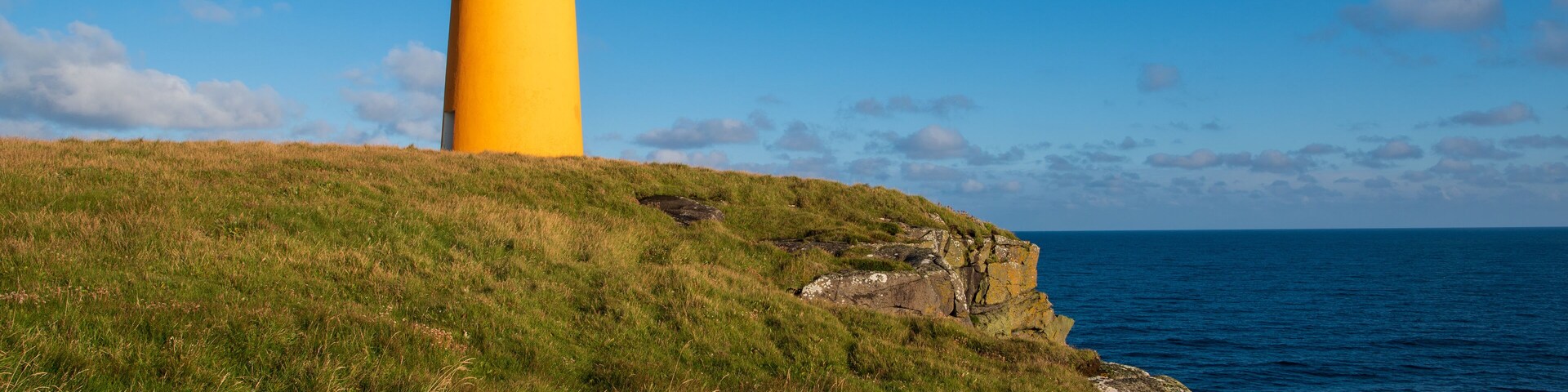 A yellow lighthouse on a grassy cliff overlooking the ocean.