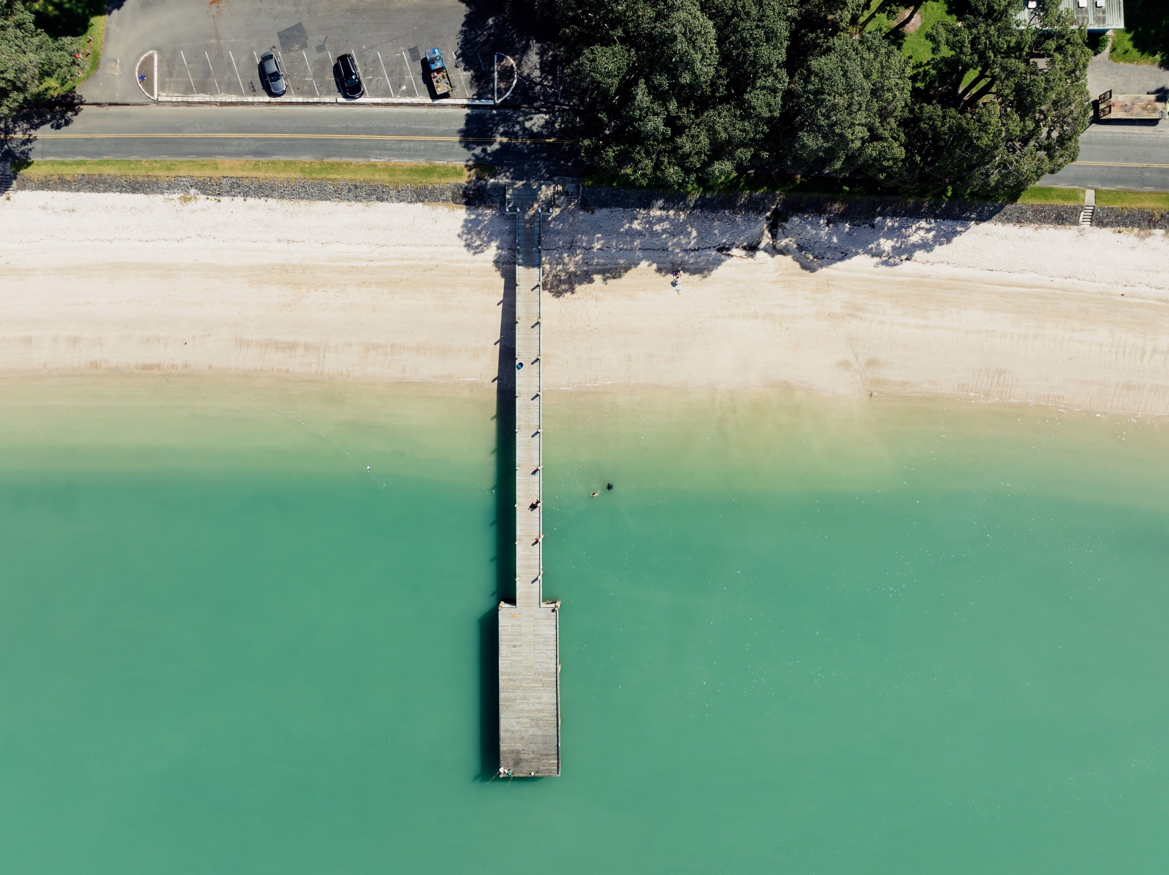 A wooden pier extending into a turquoise body of water, surrounded by a sandy beach and dense greenery.