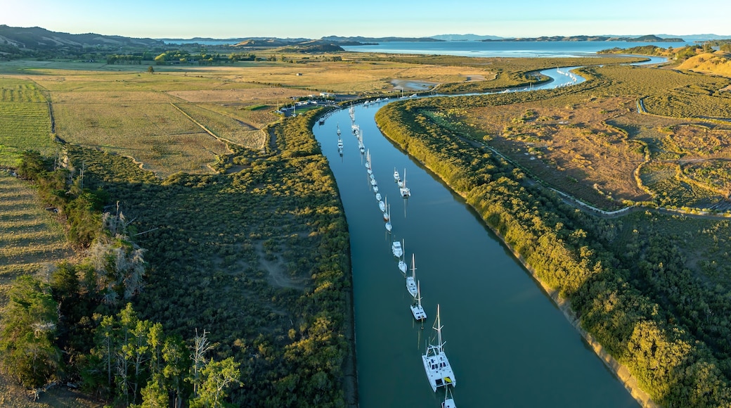 Aerial view of sailboats moored along a river in a rural landscape. The boats are lined up, reflecting in the calm water. Taken in New Zealand. CLEVEDON, NZ