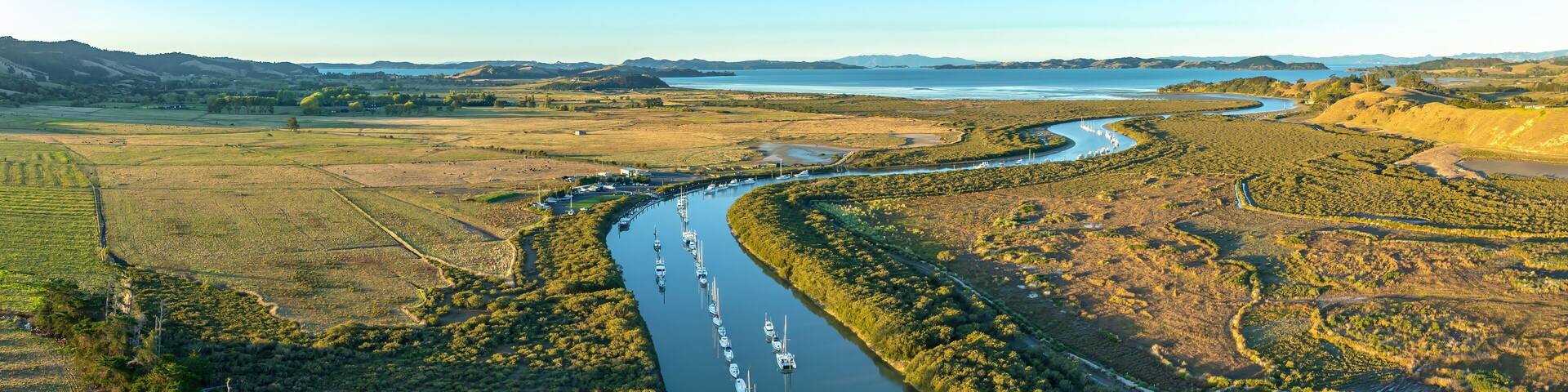 Aerial view of sailboats moored along a river in a rural landscape. The boats are lined up, reflecting in the calm water. Taken in New Zealand. CLEVEDON, NZ