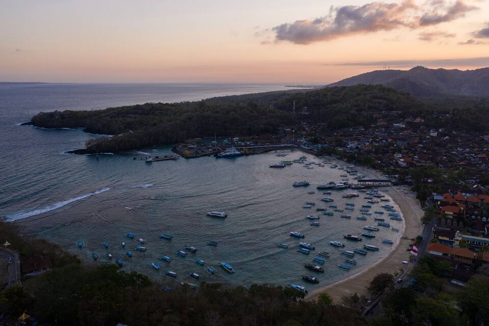 A coastal town with a marina filled with boats, a beach, and a mountainous backdrop.