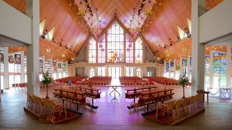 Interior de iglesia con techo de madera, vidrieras y hileras de bancas.