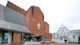 Eine Kirche mit hohem Kirchturm und ein modernes Gebäude mit Metallbedachung.