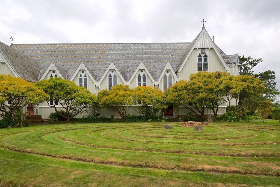 Uma igreja branca com beirais pontudos e telhado de telhas, rodeada por um jardim bem cuidado com um labirinto.