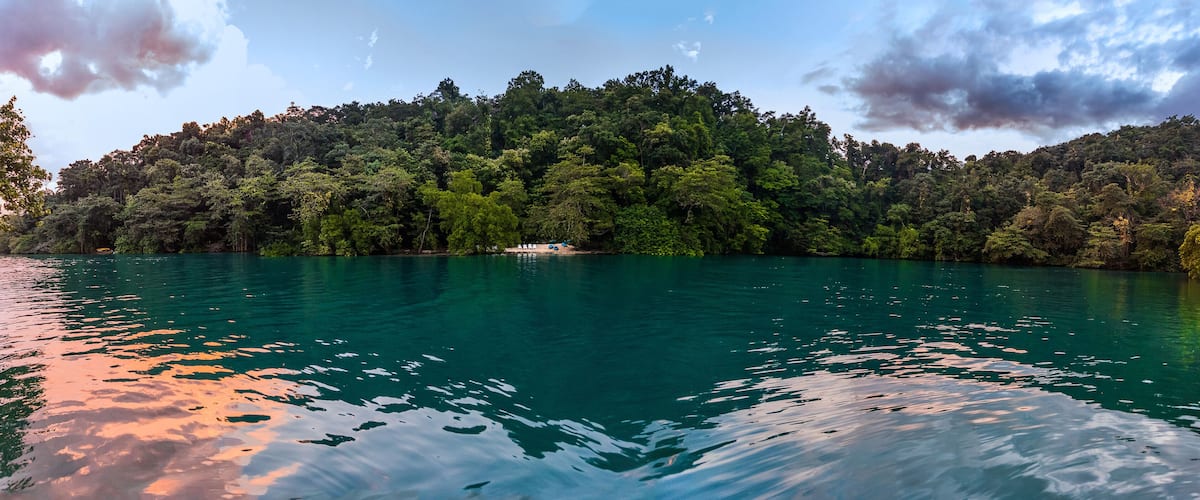 A lake surrounded by dense forest and a cloudy sky.