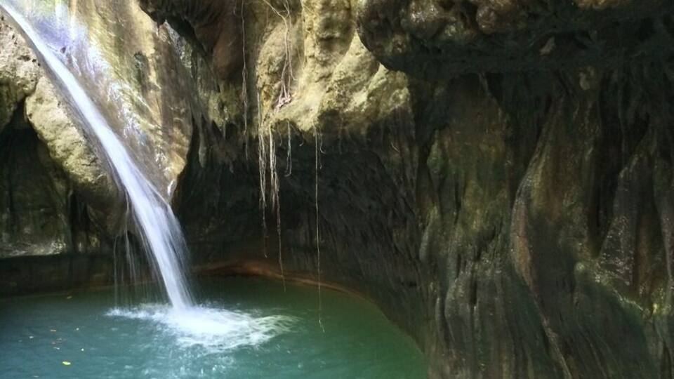 A waterfall flowing into a clear pool surrounded by rocky cliffs.