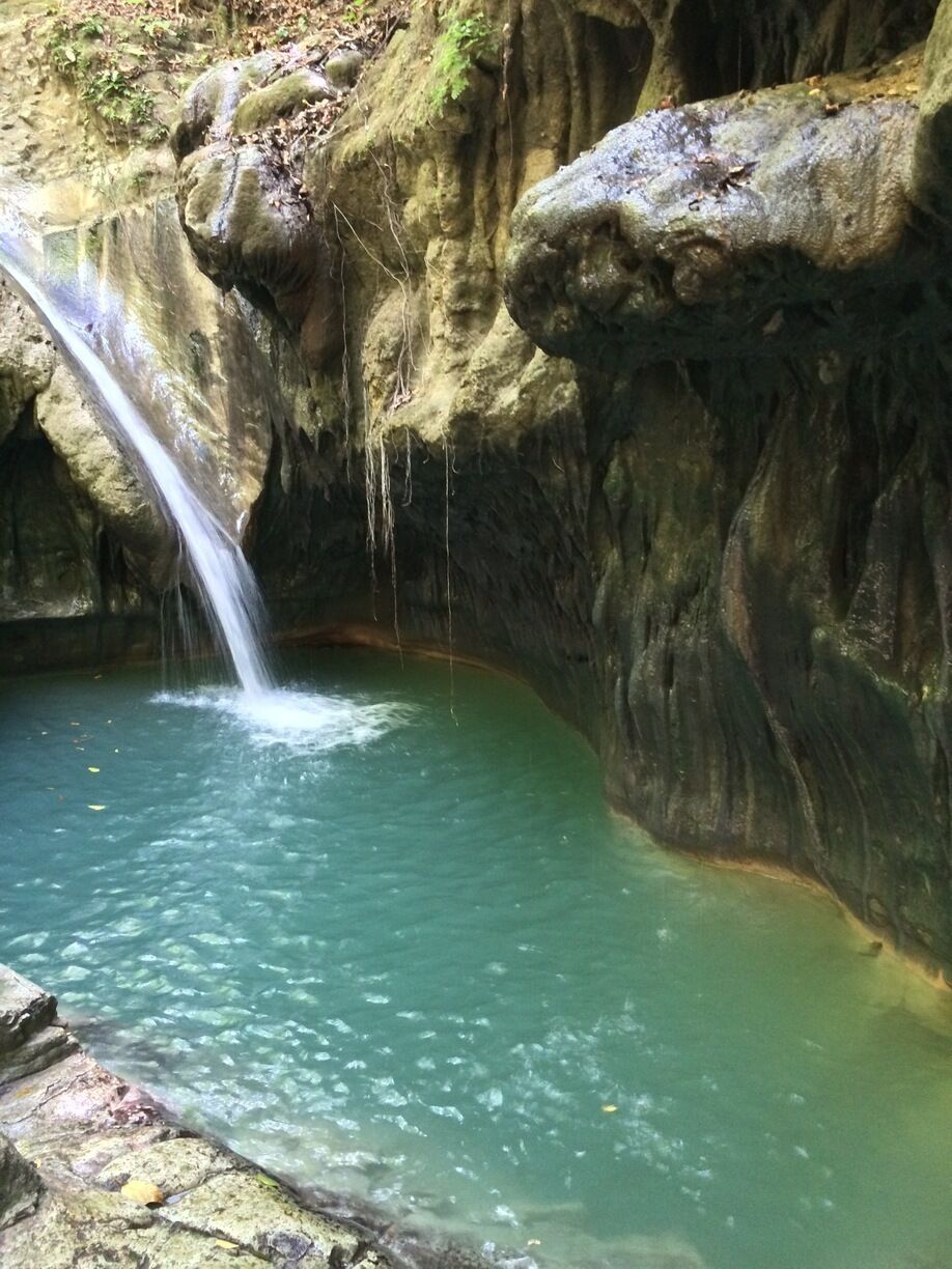 A waterfall flowing into a clear pool surrounded by rocky cliffs.