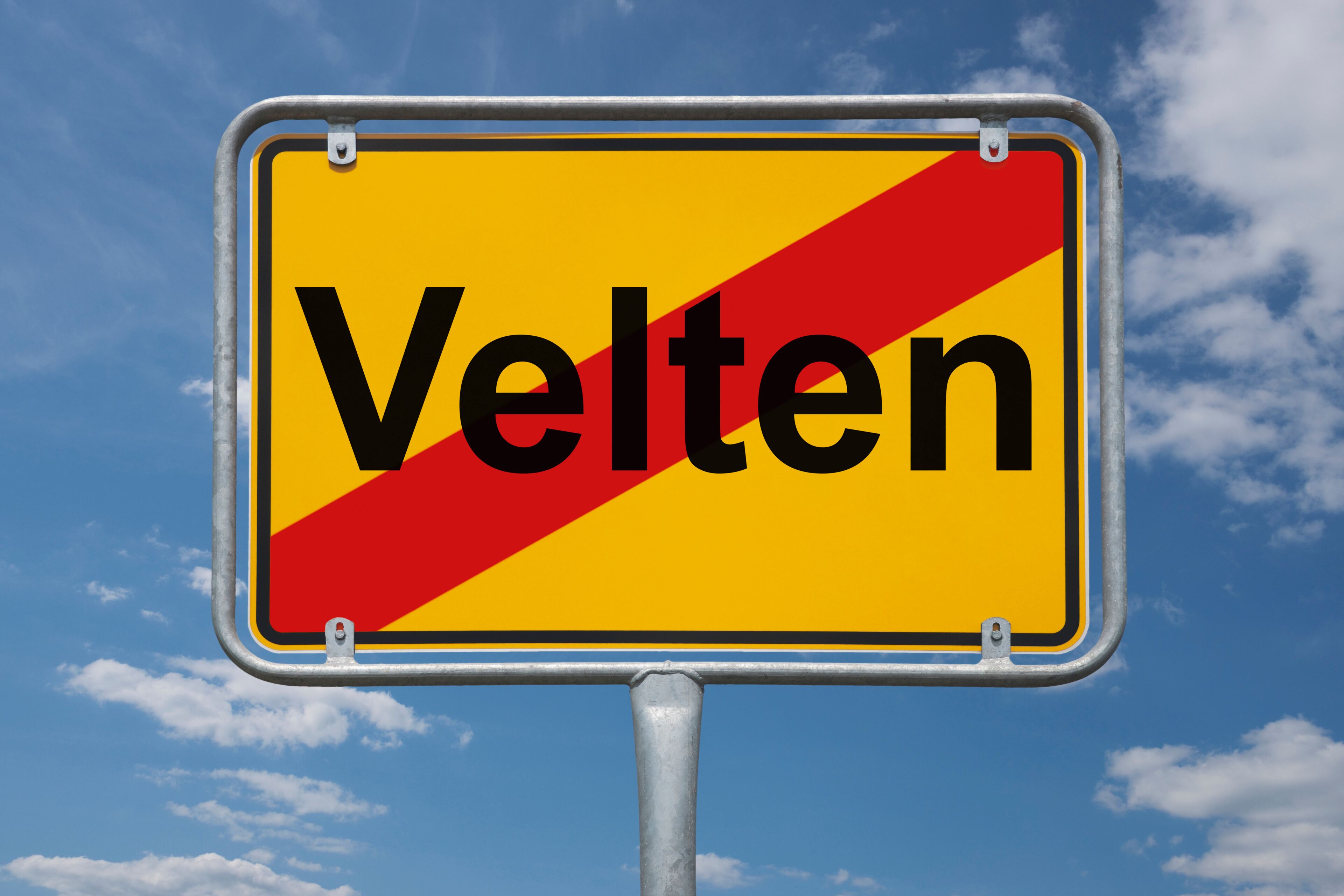 A sign with the word "Velten" against a blue sky with clouds.