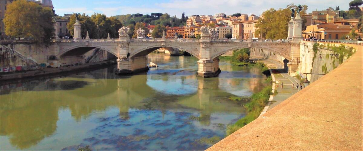 A stone bridge over a river with a cityscape in the background.
