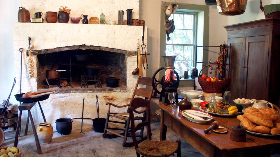 A rustic kitchen with a brick fireplace, wooden furniture, and various cooking utensils.