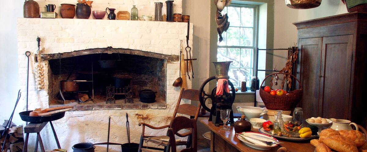 A rustic kitchen with a brick fireplace, wooden furniture, and various cooking utensils.