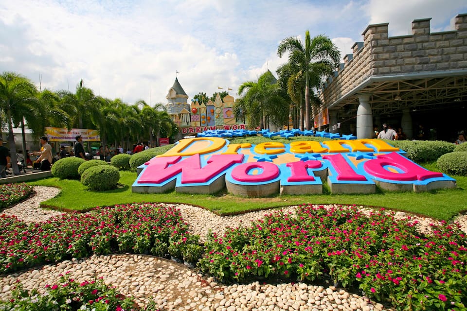 A sign for Dream World with colorful letters, surrounded by well-maintained gardens and palm trees.