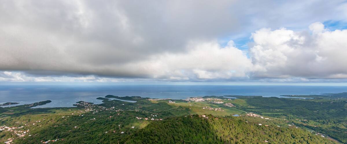 A coastal landscape with scattered houses, a large body of water, and a cloudy sky.