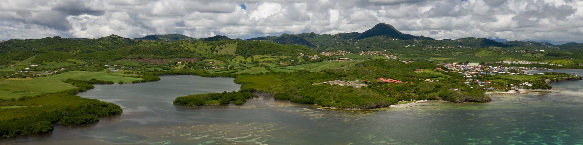 A coastal landscape with a bay, clear waters, and a mountain in the distance.