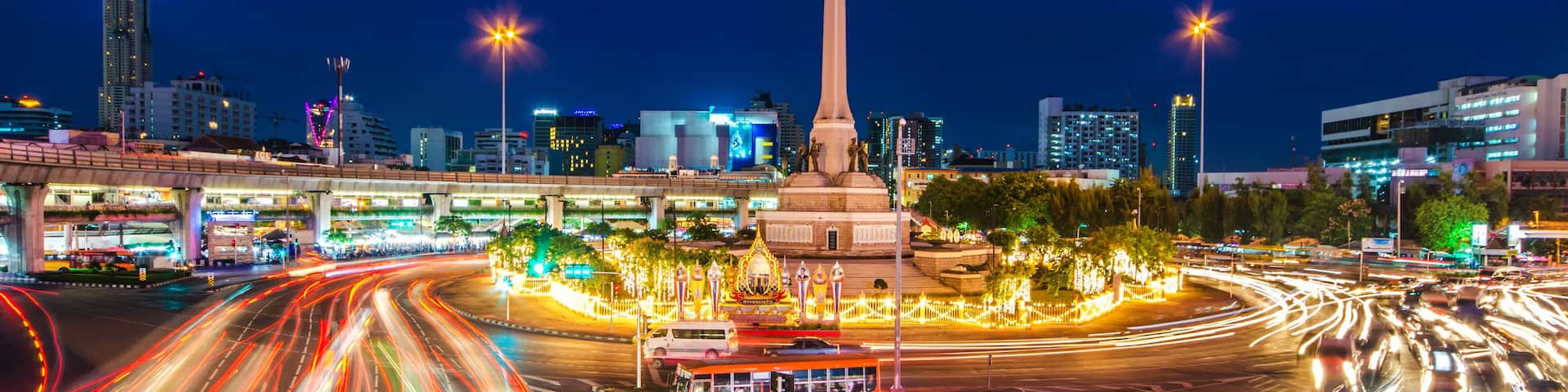 A nighttime cityscape with a prominent monument, a busy intersection with light trails from vehicles, and illuminated buildings.