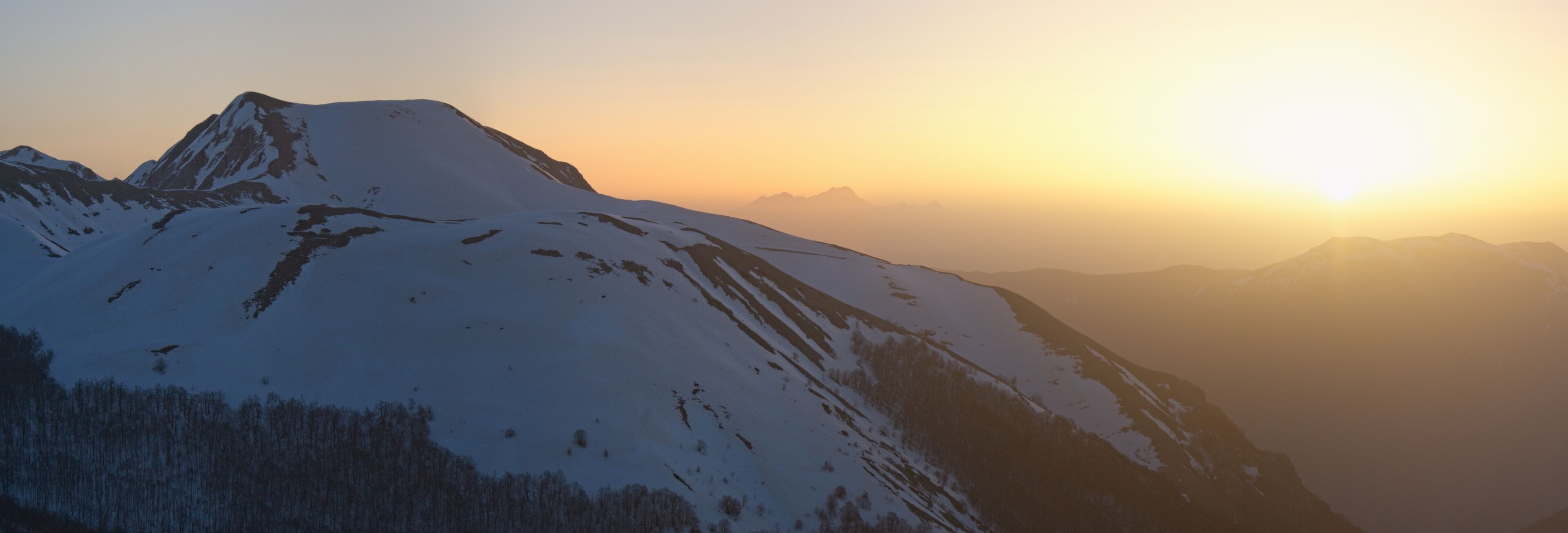 A snow-covered mountain peak during sunrise with a clear sky.