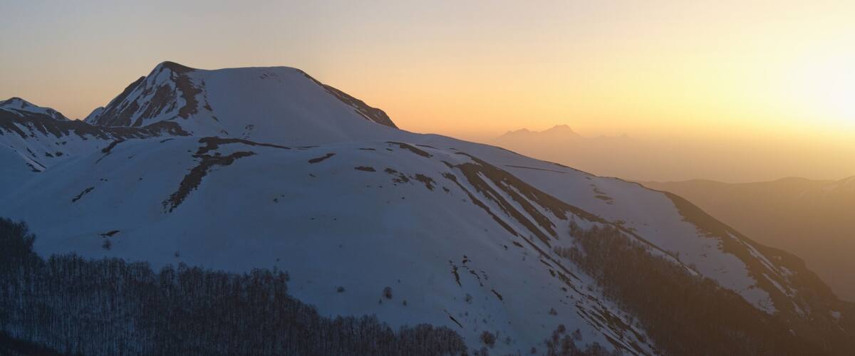 A snow-covered mountain peak during sunrise with a clear sky.