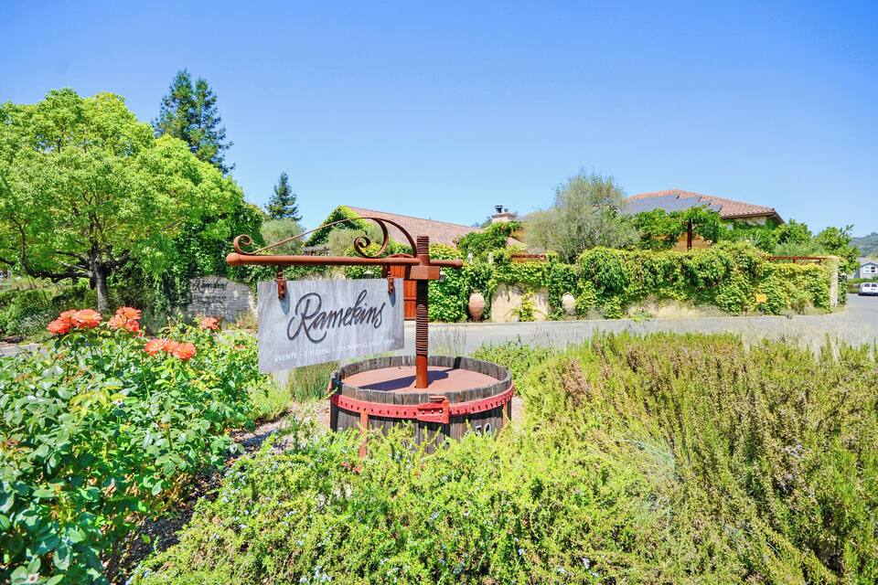 A sign for Ramkins with a decorative metal structure, surrounded by lush greenery and a clear blue sky.