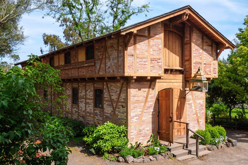 A rustic wooden building with a brick facade, surrounded by lush greenery and trees.