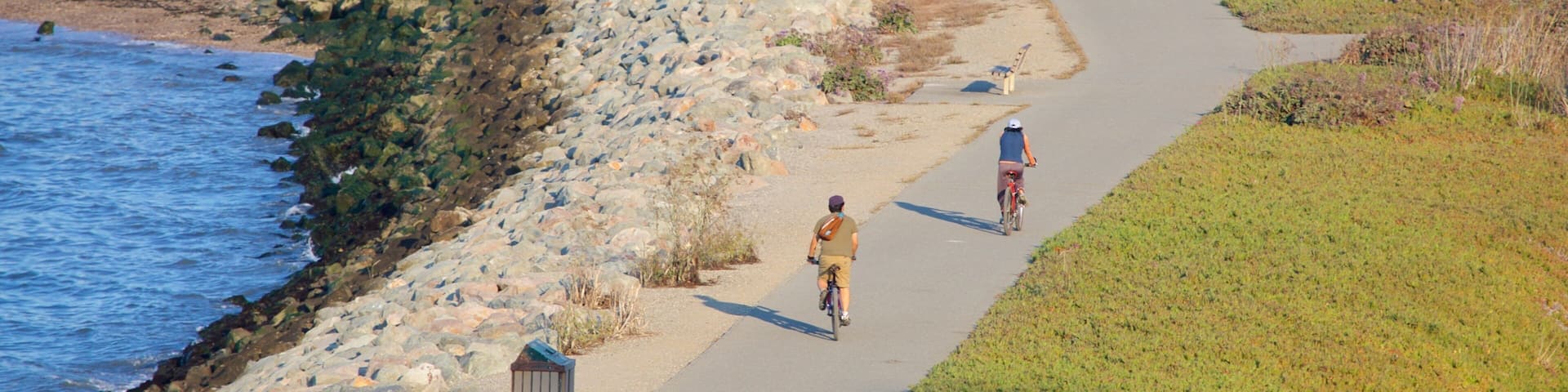 A coastal path with a rocky shoreline, a bench, and a sign.