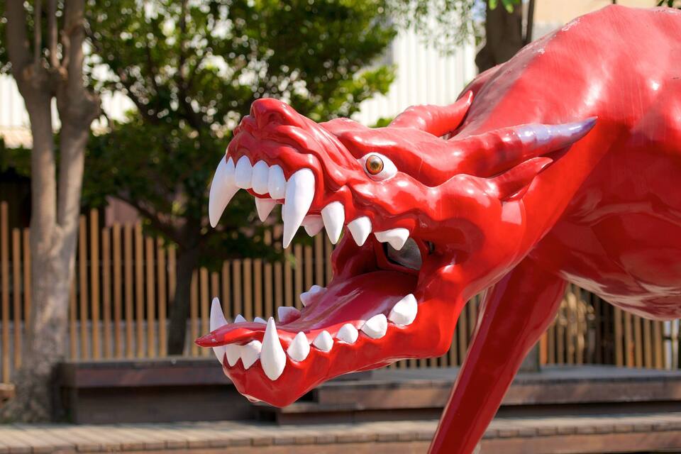 A red dinosaur statue with sharp teeth and a menacing expression.