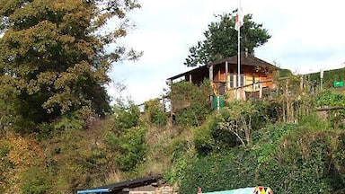 Um barco preto com decorações coloridas atracado perto de uma casa numa colina.