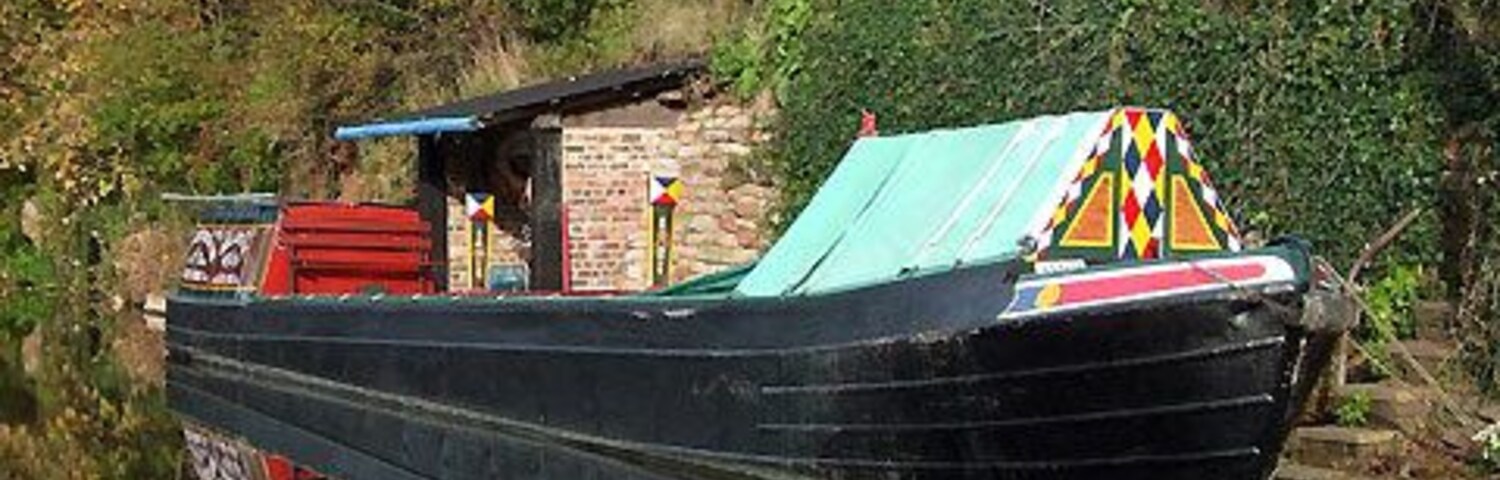 Um barco preto com decorações coloridas atracado perto de uma casa numa colina.