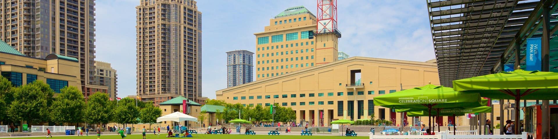 A city square with a large green lawn, picnic tables, and a clock tower.