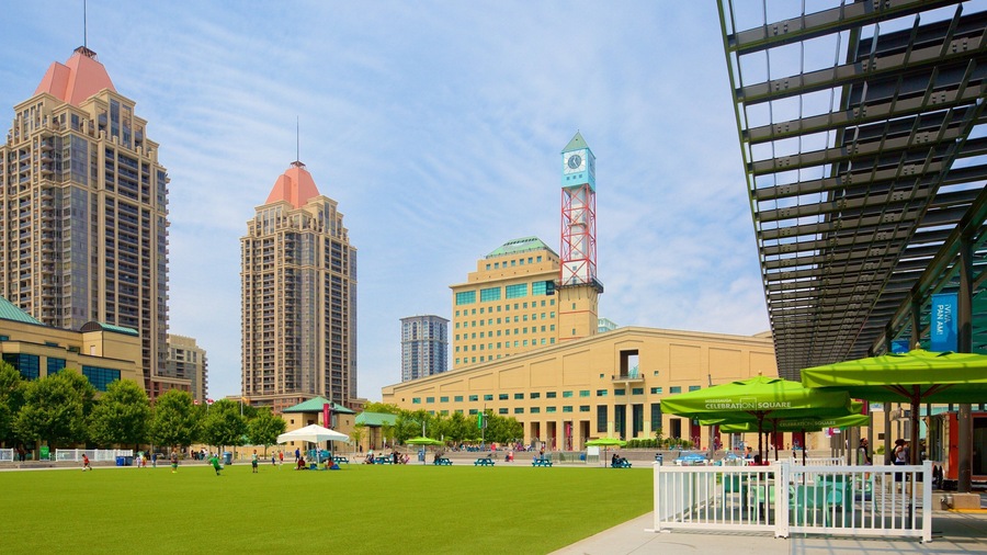A city square with a large green lawn, picnic tables, and a clock tower.
