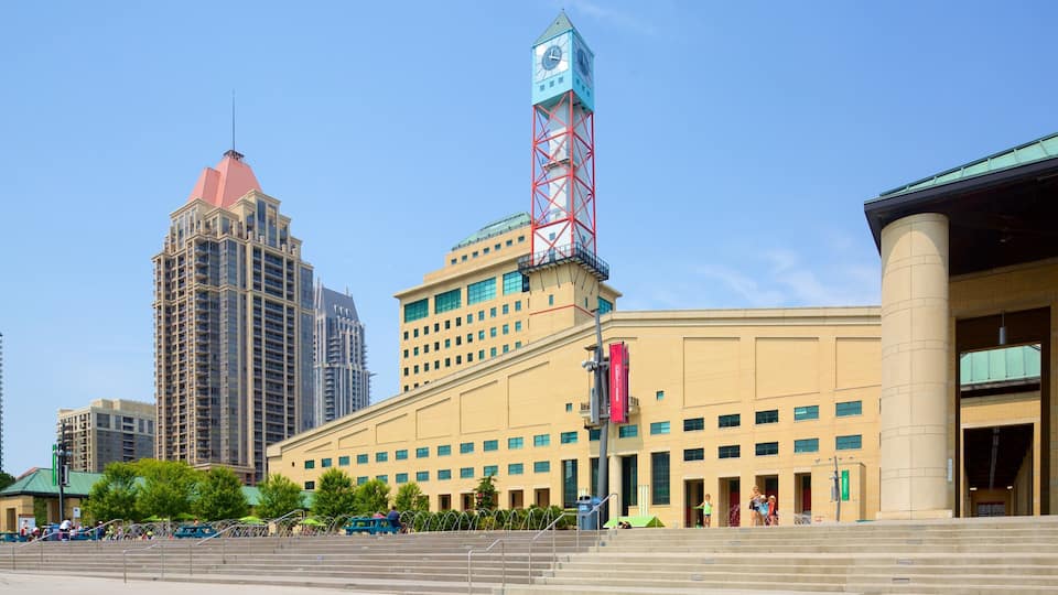 A cityscape with a prominent clock tower, modern high-rise buildings, and a large public building with steps leading up to it.