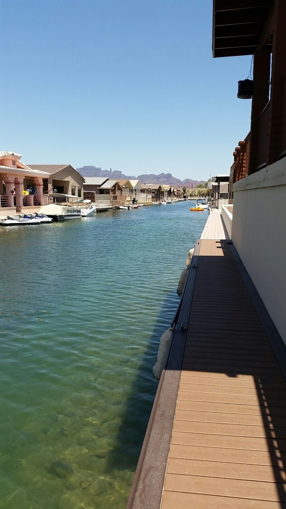 A marina with boats docked, a wooden walkway, and buildings in the background.