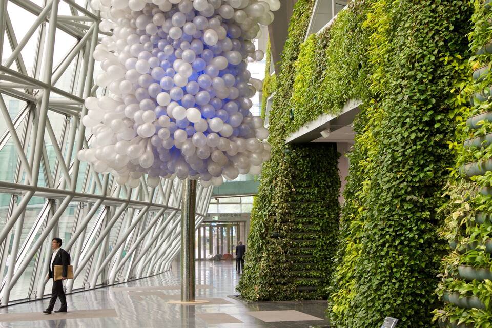 A modern building interior with a glass facade, a large white and blue balloon installation, and a vertical garden wall.