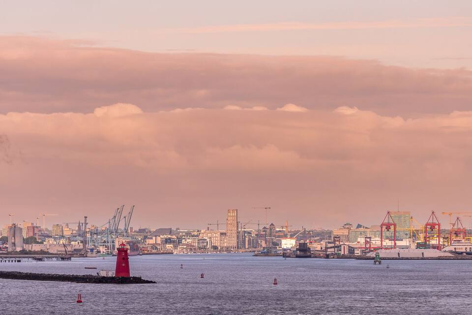 A harbor with a red lighthouse, industrial buildings, and cranes.