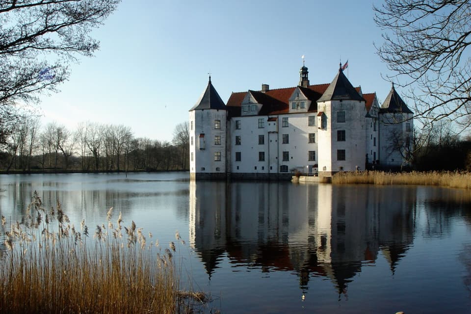 Un grande castello bianco con numerose torri affacciato su un lago tranquillo.