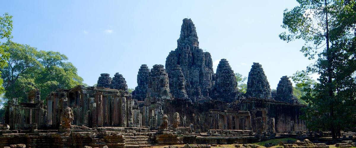 Ancient stone ruins with multiple towers and statues, surrounded by trees and a clear sky.