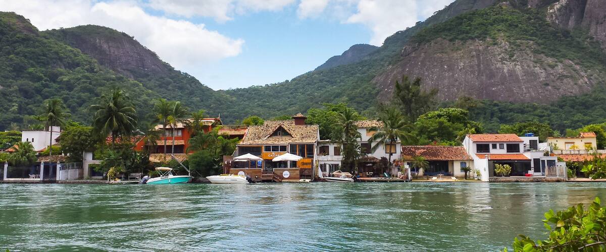 A coastal village with buildings, boats, and lush green mountains in the background.