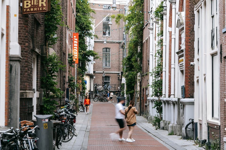 A narrow street lined with brick buildings, bicycles parked along the sides, and pedestrians walking.