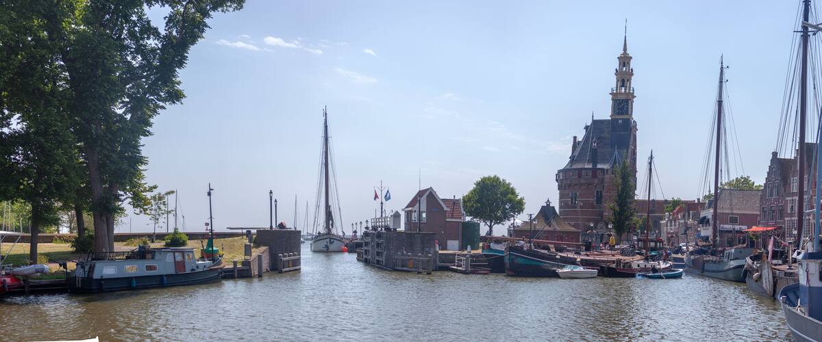 A canal with boats docked, a prominent tower, and historic buildings along the water.