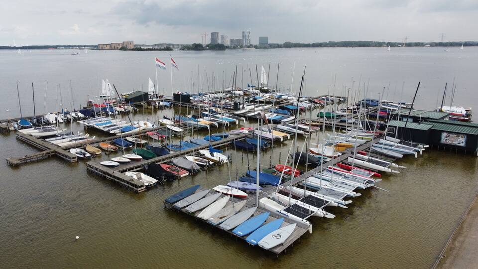 A marina with numerous boats docked, a city skyline in the background, and a cloudy sky.