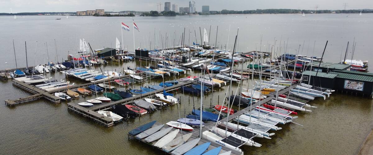 A marina with numerous boats docked, a city skyline in the background, and a cloudy sky.