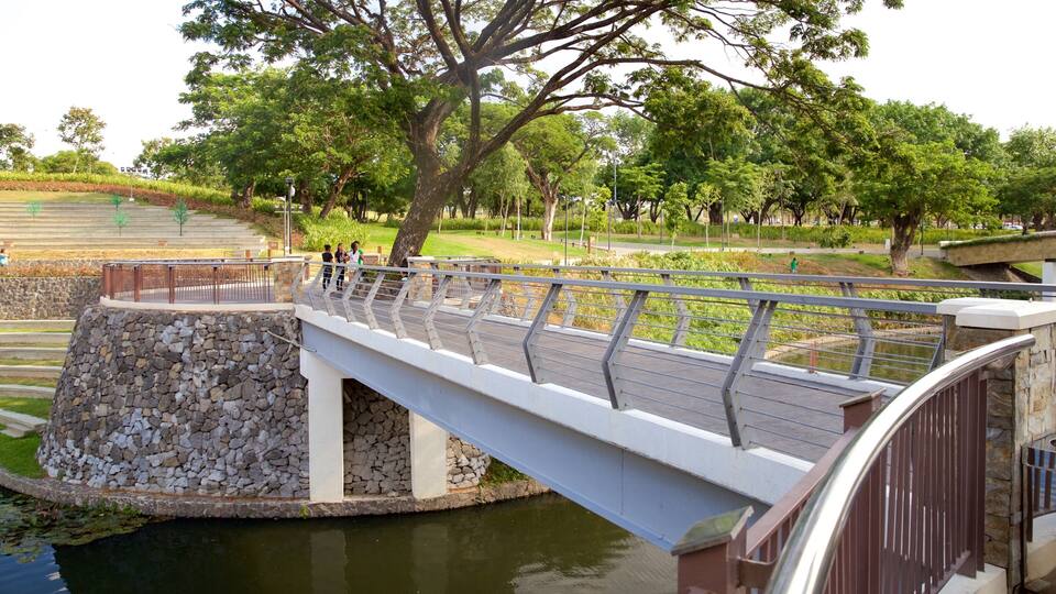 A stone bridge over a pond with trees and a park in the background.