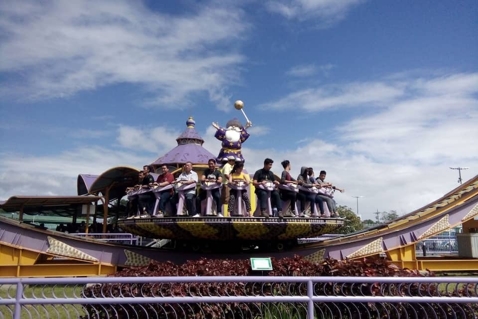 A carousel with riders and a purple-roofed structure in the background.