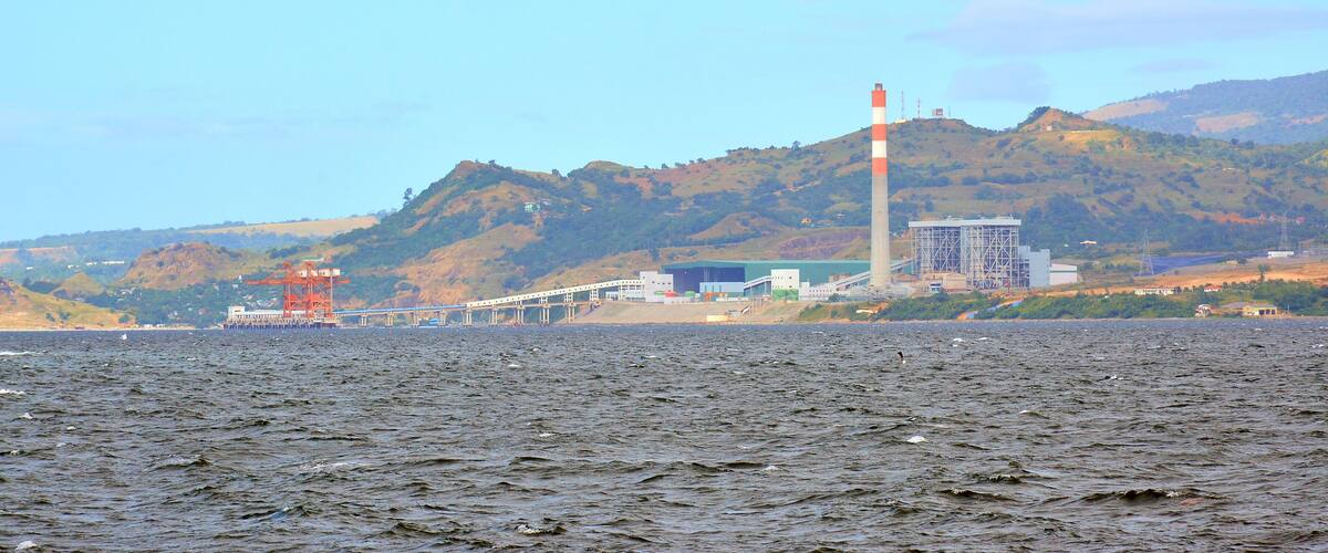 A coastal landscape with a bridge, a lighthouse, and industrial buildings.