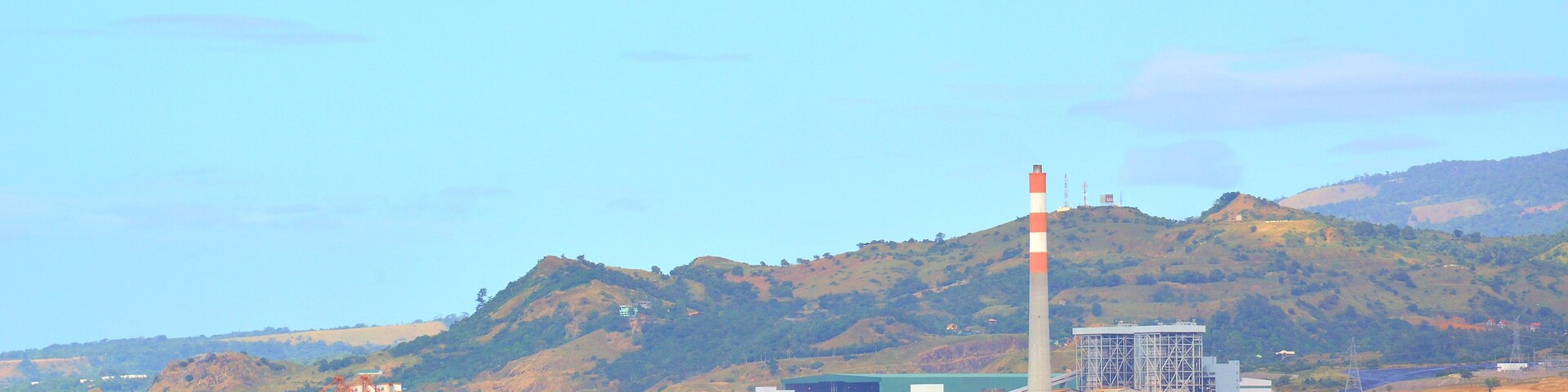 A coastal landscape with a bridge, a lighthouse, and industrial buildings.